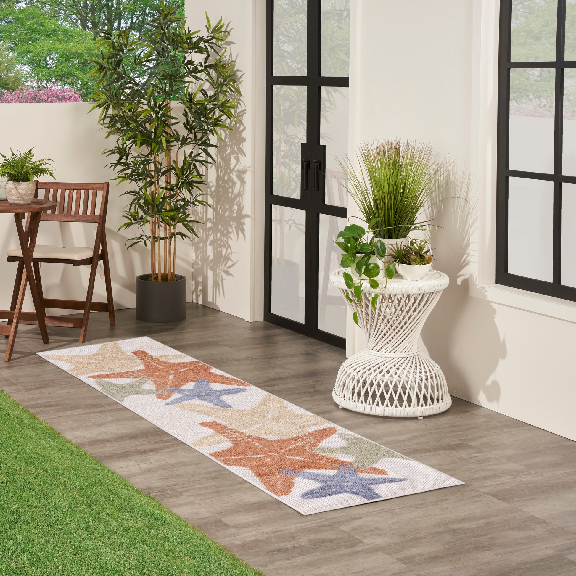 Outdoor runner rug with coral and blue starfish pattern on a porch with plants and glass doors.