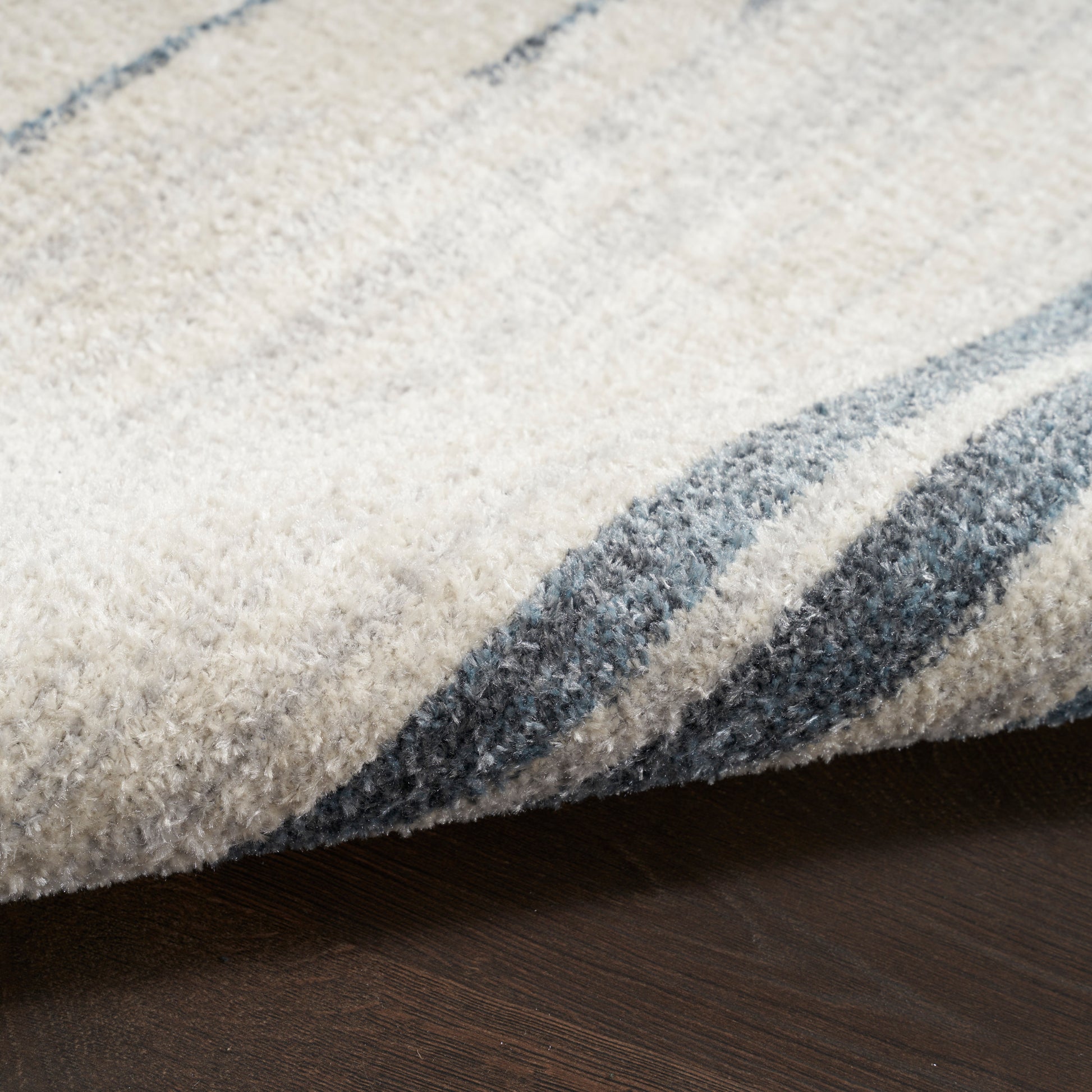 Cream and blue striped plush rug with soft pile and folded edge on dark wood floor.