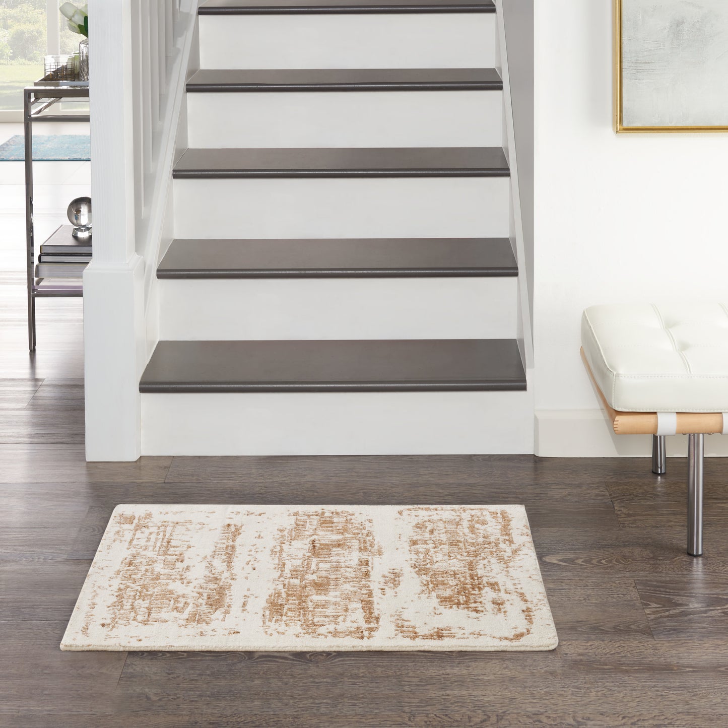 Modern entryway: white staircase with dark wood treads, beige patterned rug, white bench with chrome legs.