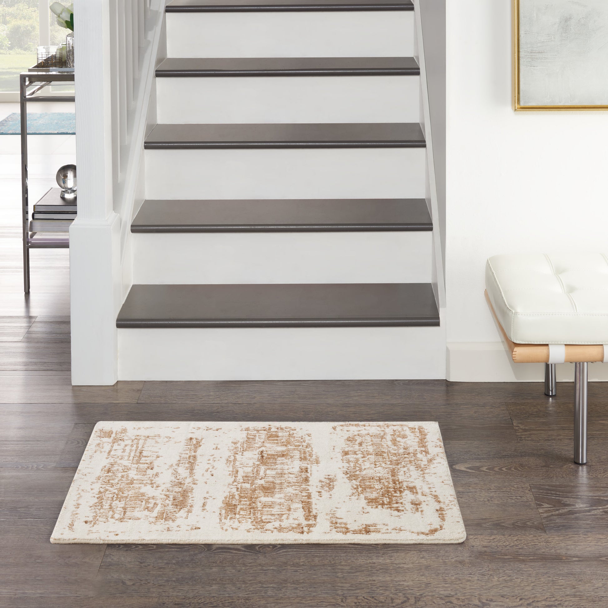 Modern entryway: white staircase with dark wood treads, beige patterned rug, white bench with chrome legs.
