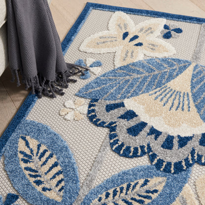 Blue and cream floral/leaf patterned woven area rug on light wood floor, with a gray fringed throw nearby.