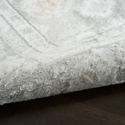 Close-up of a soft light-gray shag rug with thick fluffy pile and subtle pattern on a dark wood floor.