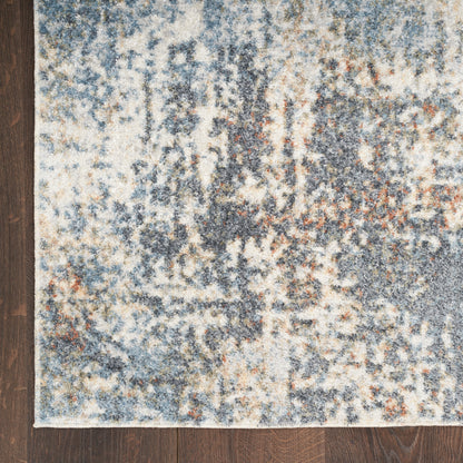 Abstract blue-gray rectangular area rug with beige and rust accents on dark wood floor.