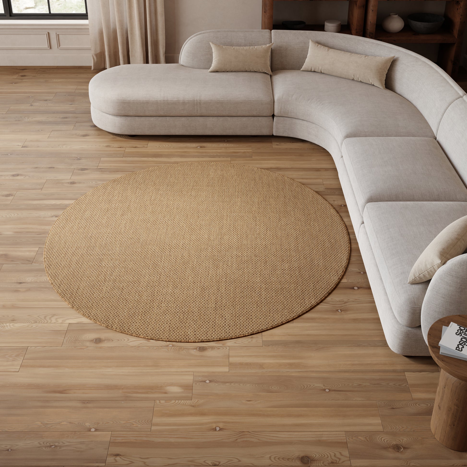 Curved beige fabric sectional with cream cushions around a round natural jute rug on wooden floor.