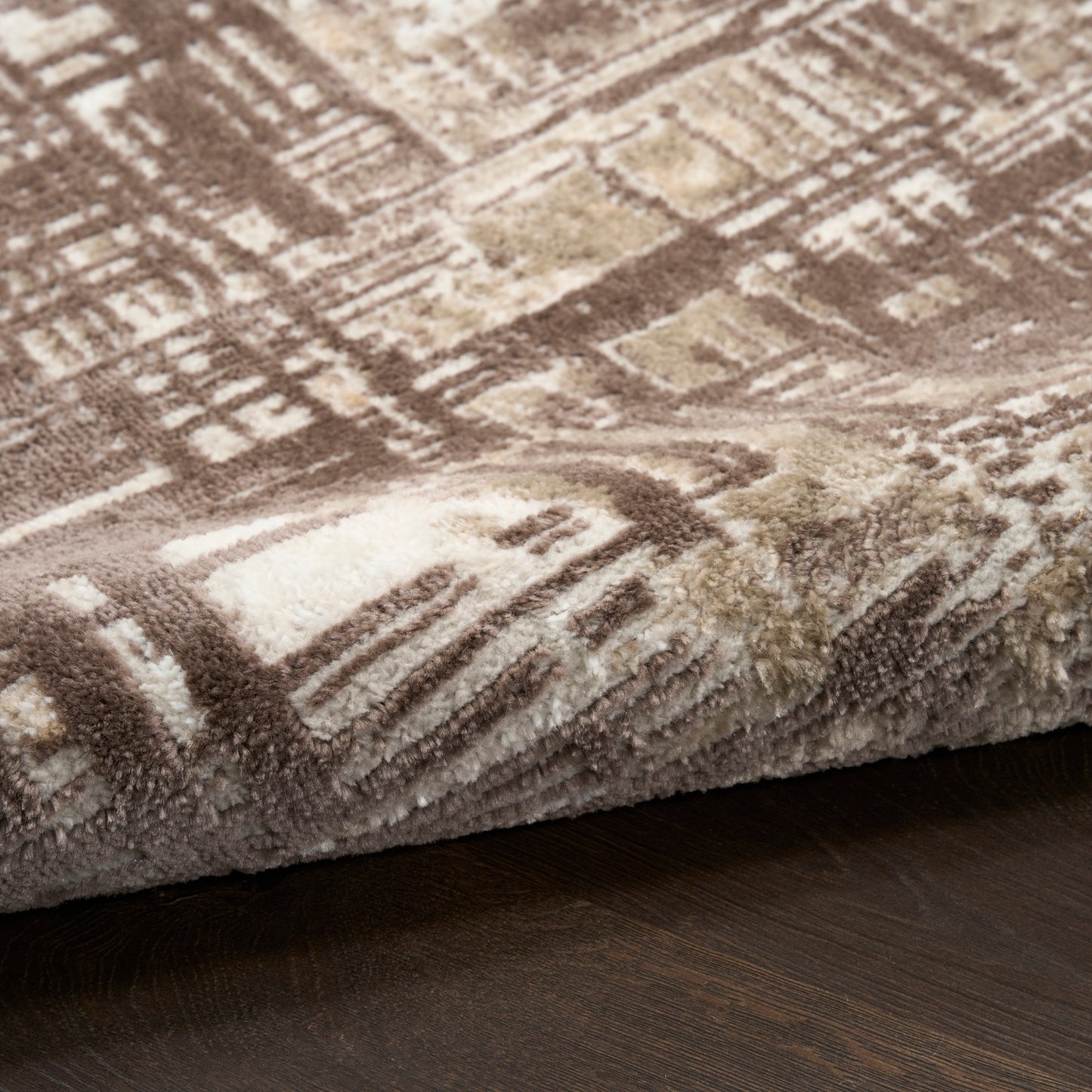 Close-up of a shaggy geometric rug in brown, cream and beige tones folded over a dark wood floor.