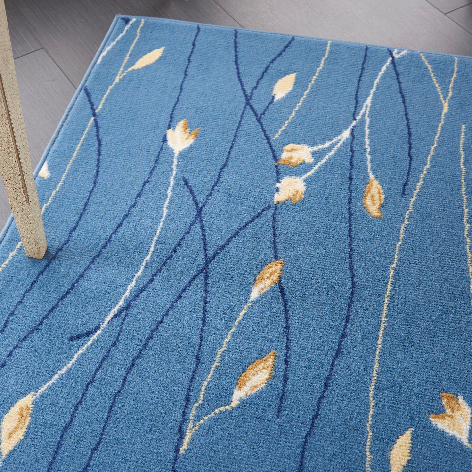 Blue area rug with navy curved lines and golden leaf motifs on soft pile, laid on wood floor.