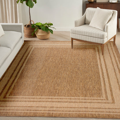 Rectangular natural jute area rug with beige border in a bright living room with cream sofa and striped armchair.
