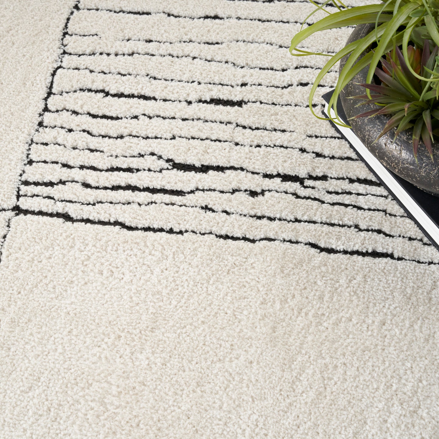 Cream shag rug with black abstract stripes; plush pile, modern minimalist decor beside a potted plant.