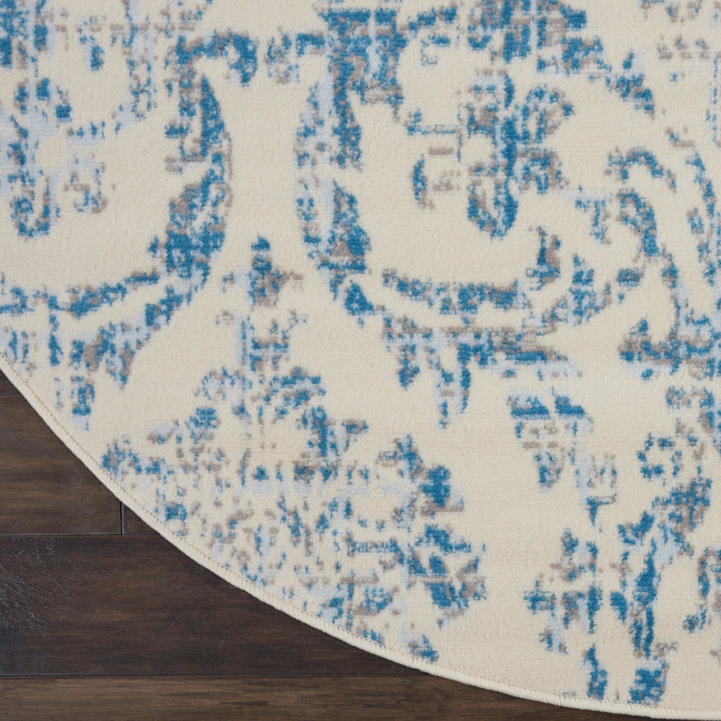 Round cream rug with blue abstract pattern on dark wood floor.