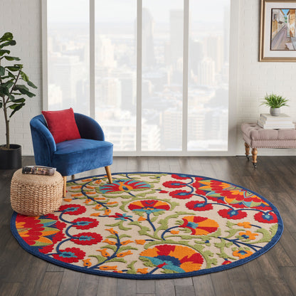 Colorful round floral area rug with blue border, placed in a modern living room beside a blue velvet chair.