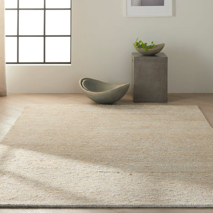 Natural jute rug in a minimalist room with a curved gray-green ceramic bowl and a concrete pedestal with a small plant.