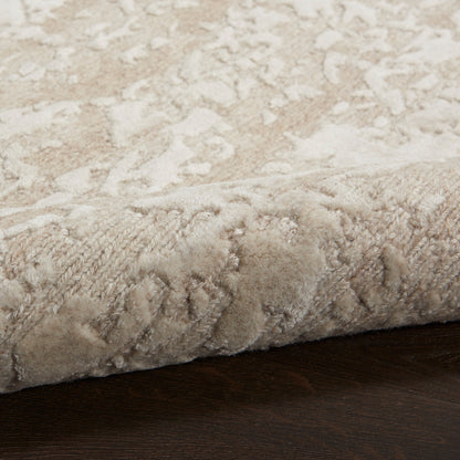 Beige textured area rug with subtle damask pattern, rolled edge resting on dark wood floor.