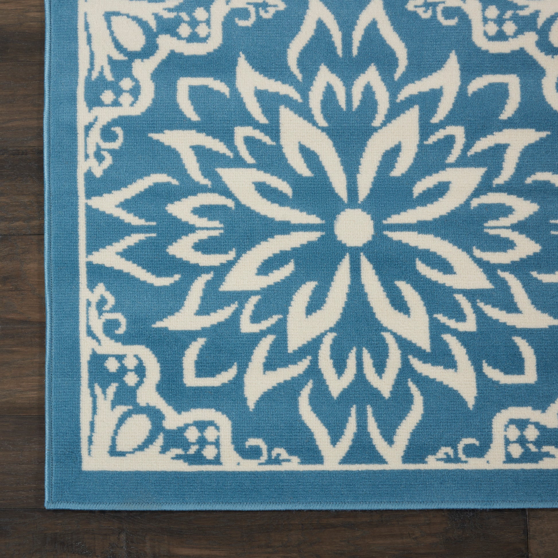 Blue area rug with a large white mandala floral pattern and a light blue border on dark wood floor.