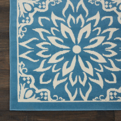 Blue area rug with a large white mandala floral pattern and a light blue border on dark wood floor.