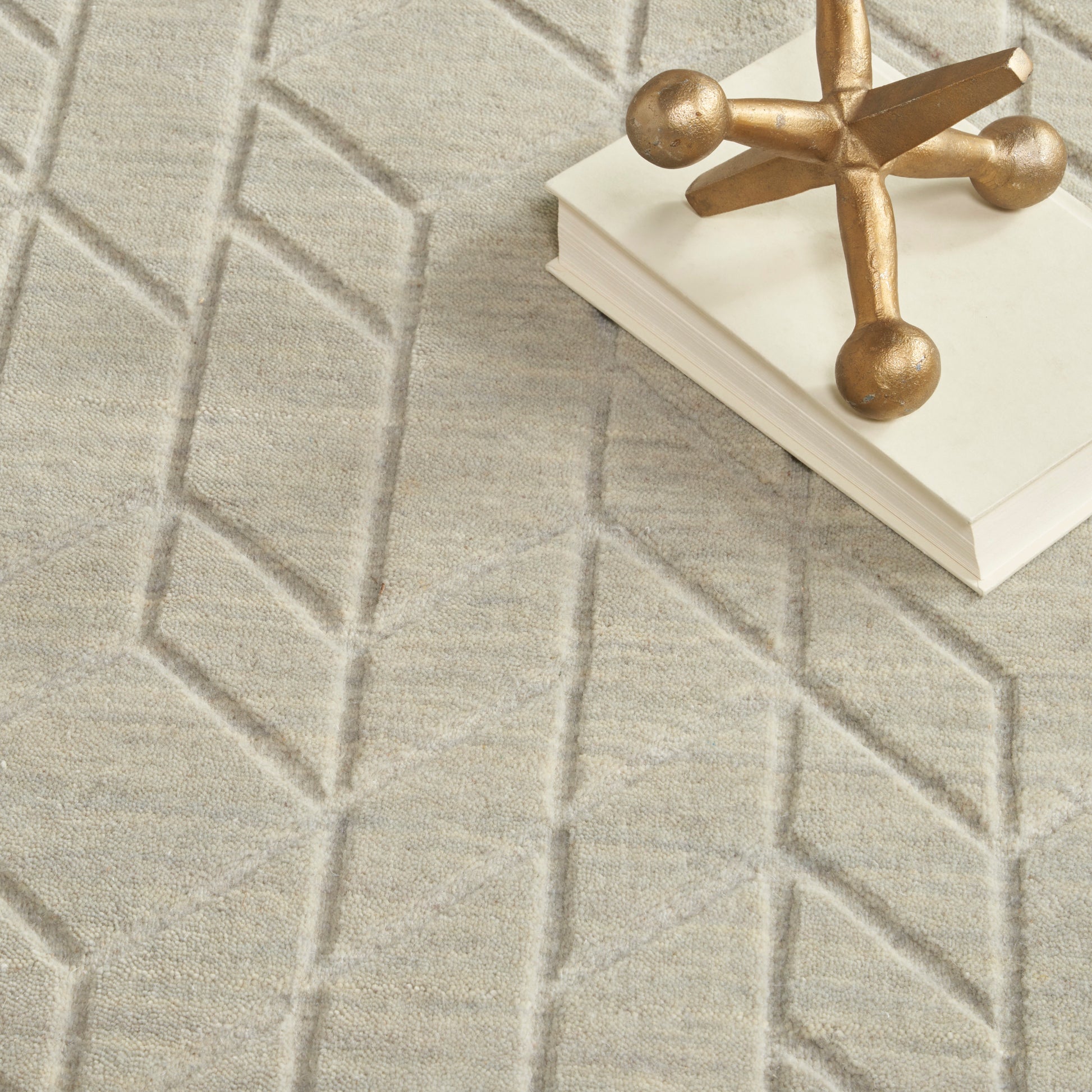 Beige geometric rug with raised diamond pattern; white book stack topped by a gold decorative cross.