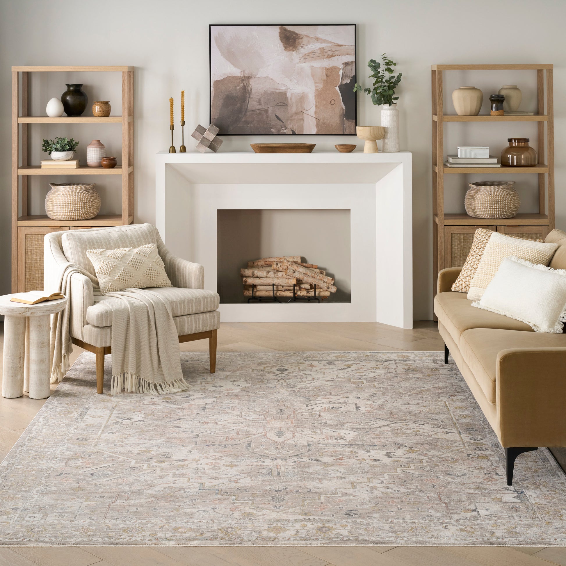 Cozy neutral living room with white geometric fireplace, beige sofa and armchairs, wood bookshelves, abstract art, woven rug.