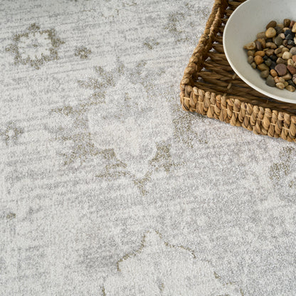 Light gray textured rug with faded ornate trellis pattern; wicker basket and white bowl of mixed pebbles.