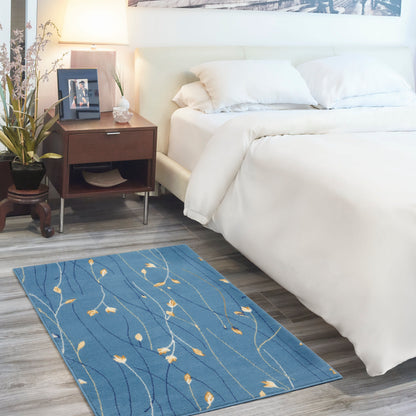 Blue rug with yellow leaf motifs & white wavy lines in a modern white bedroom beside a bed & nightstand.
