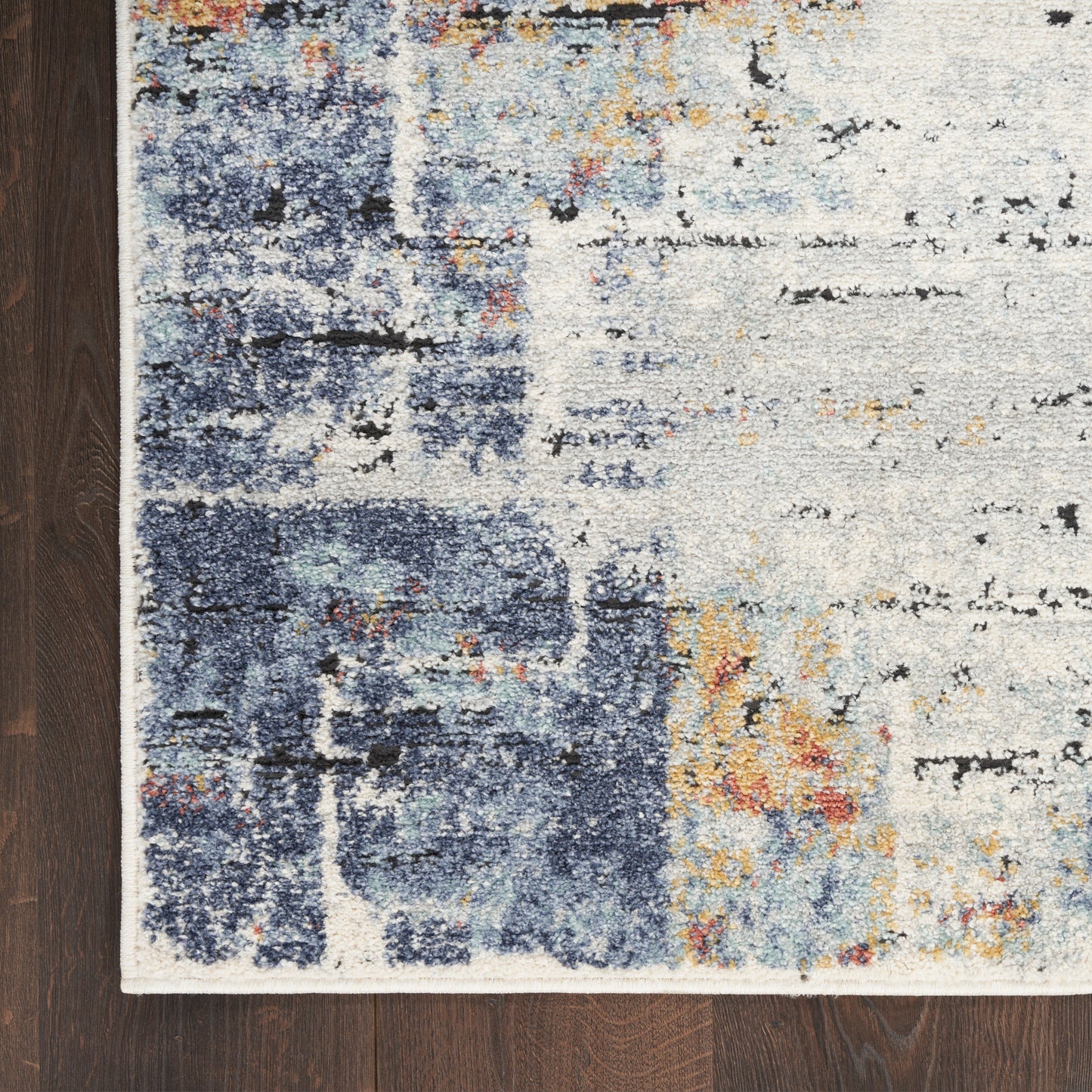 Abstract blue, cream and gray rug corner with orange specks; distressed modern pattern on dark wood floor.