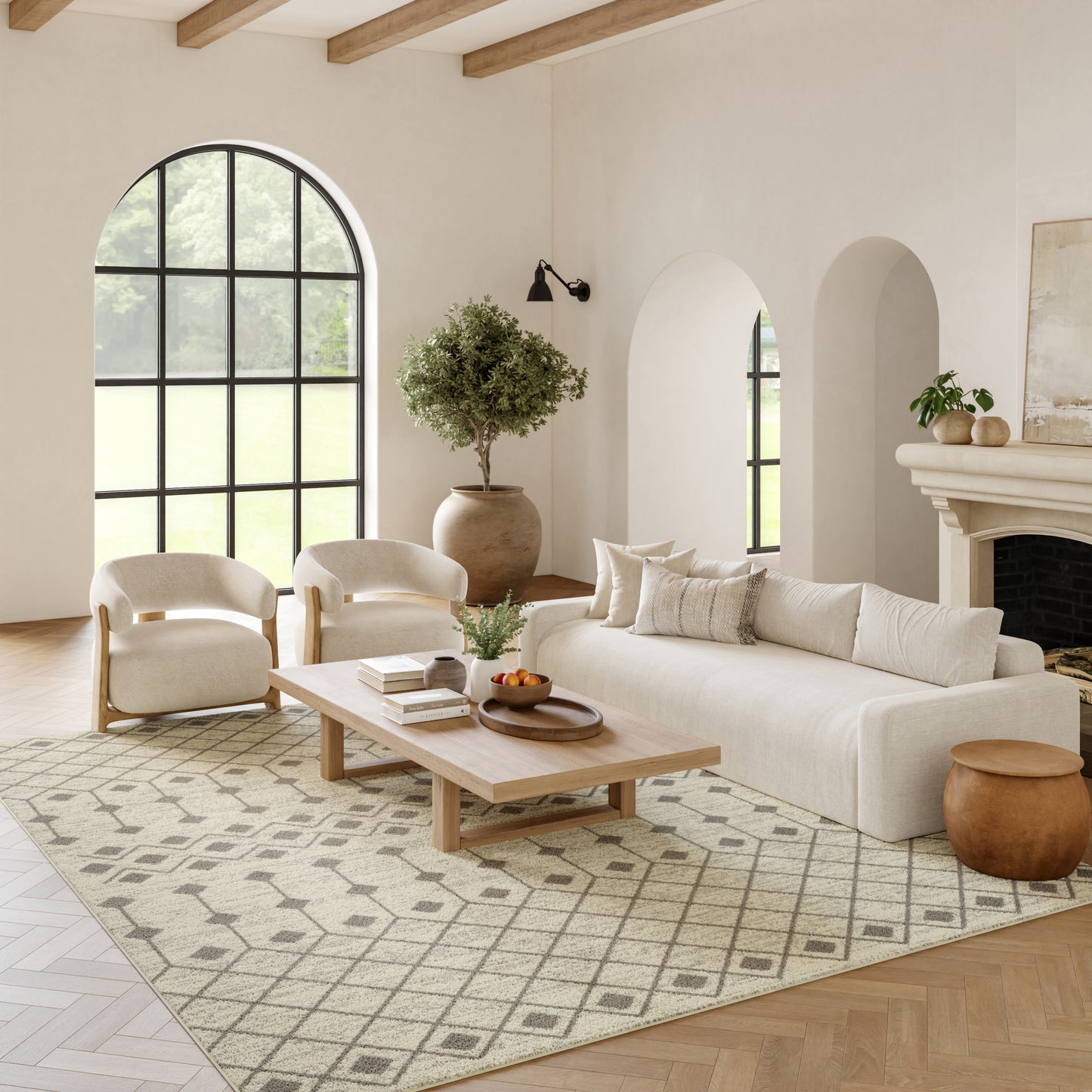 Bright living room with cream sofa and chairs, light wood coffee table, arched window, rug, potted tree, fireplace.