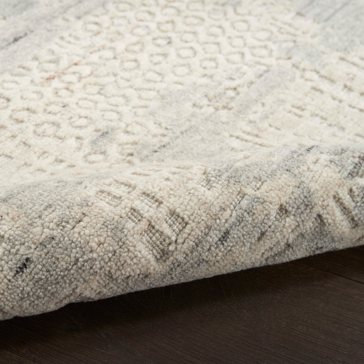 Beige cream geometric patterned area rug with soft textured pile; folded edge on dark wood floor.