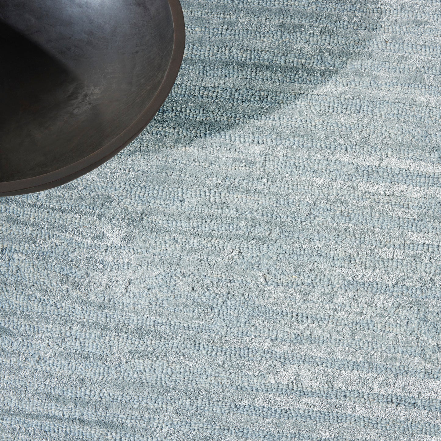 Partial view of a black round frying pan on a blue textured rug.