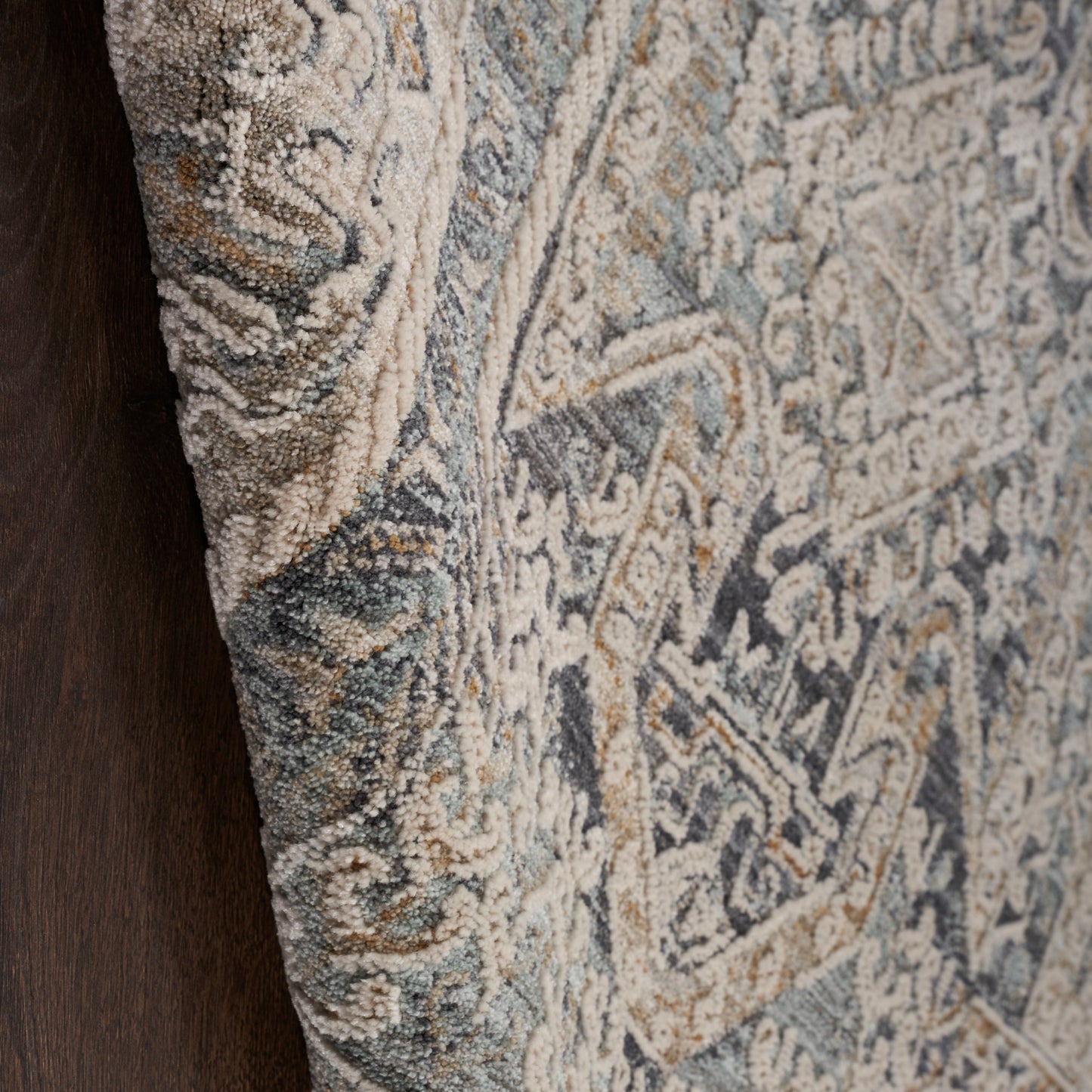 Close-up of a textured wool runner rug with blue, beige and gray floral patterns; dark wood edge visible.