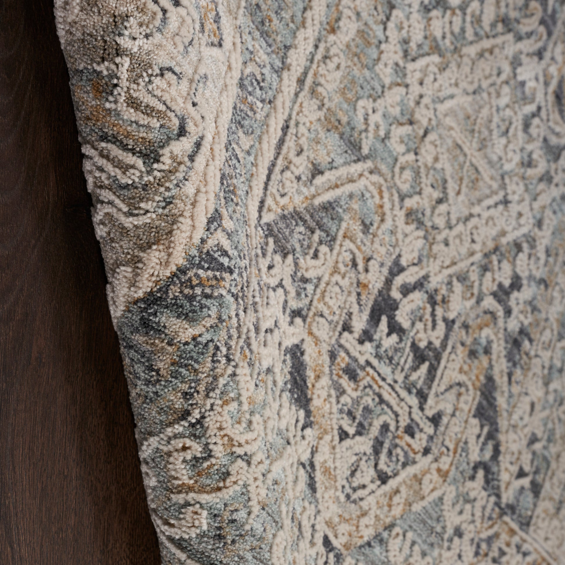 Close-up of a textured wool runner rug with blue, beige and gray floral patterns; dark wood edge visible.