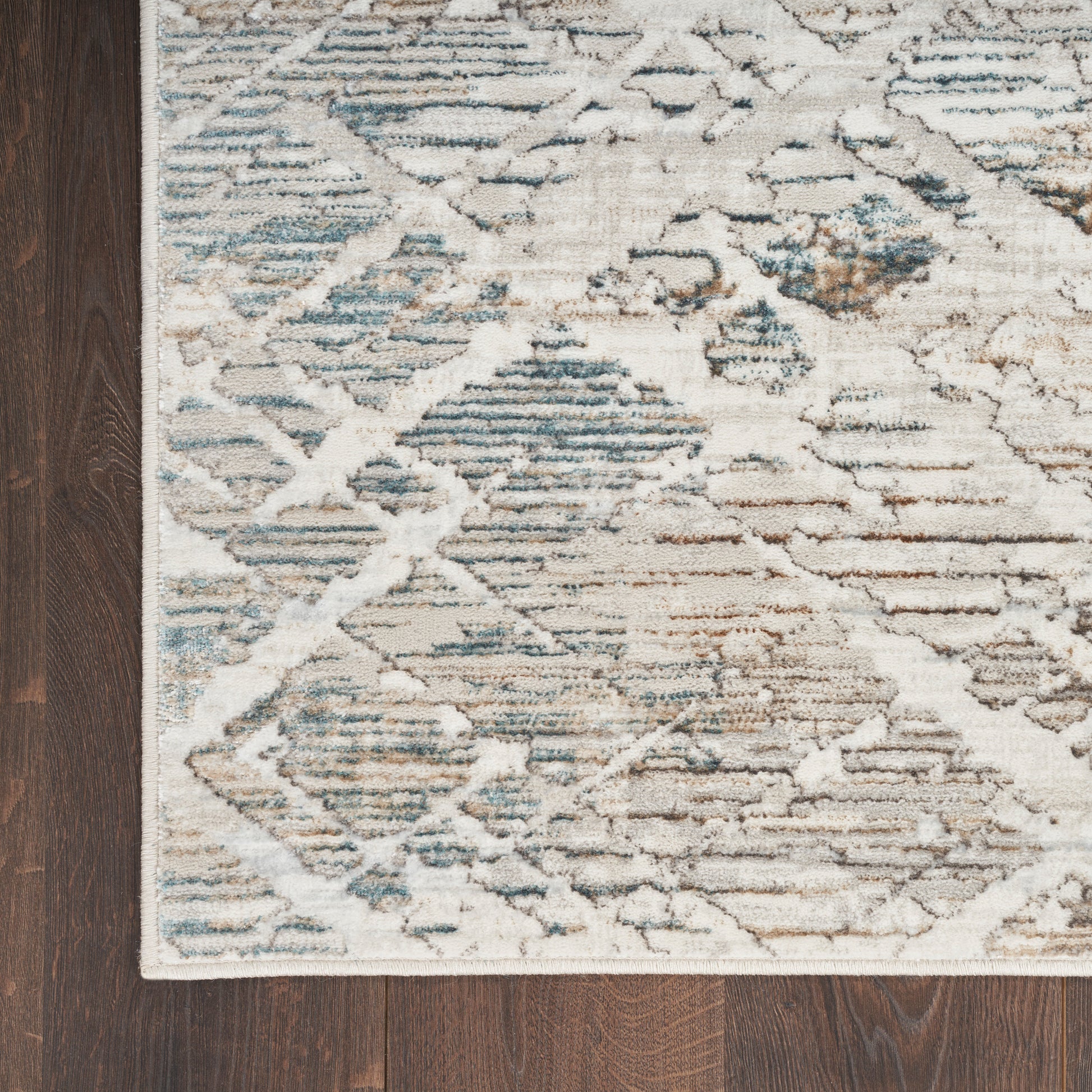 Cream and blue geometric area rug with taupe accents on dark wood floor.
