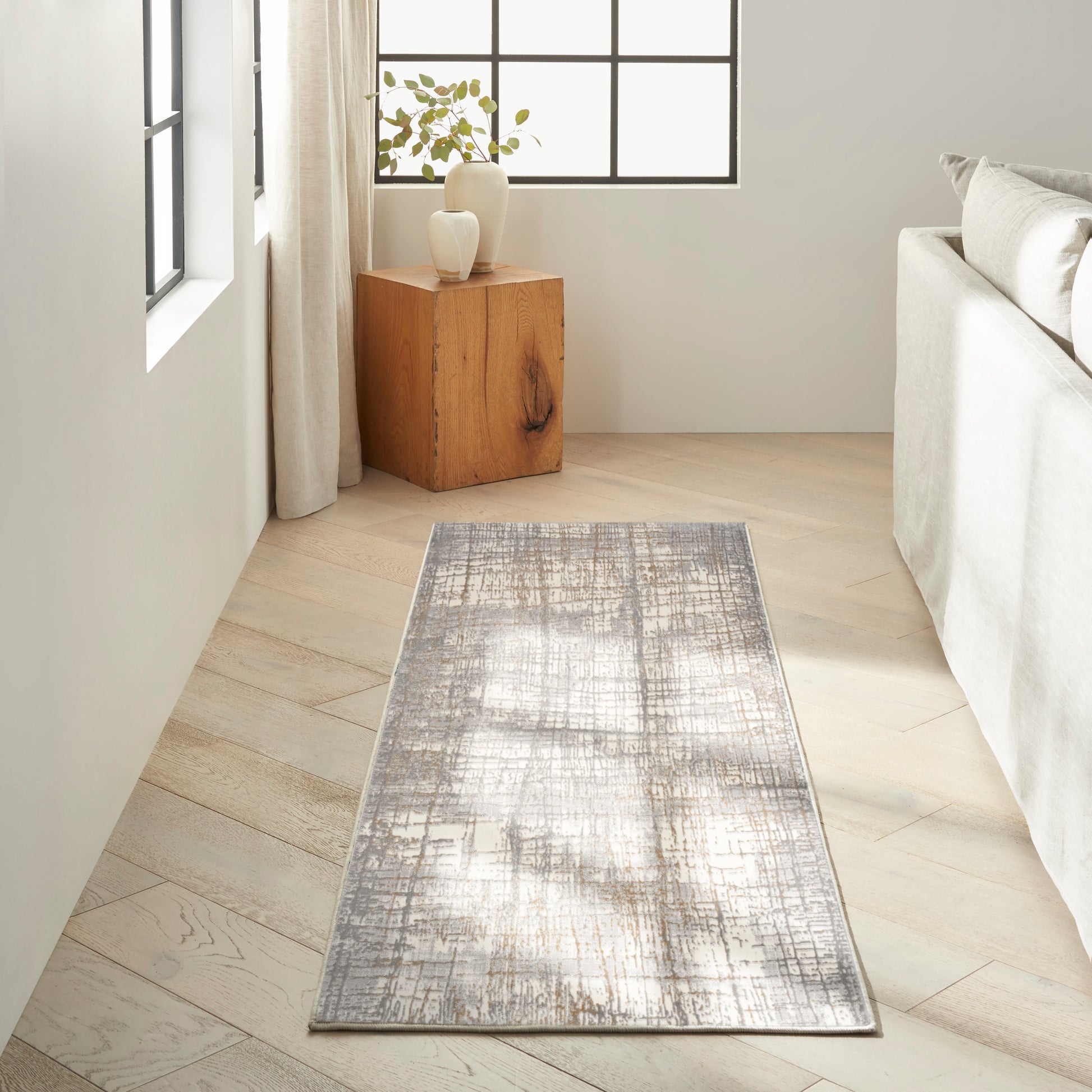 Textured gray distressed runner rug on light wood floor beside a gray sofa in a modern minimalist living room.