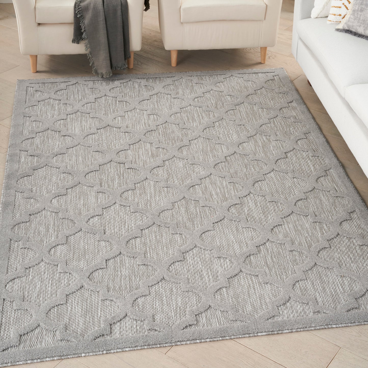 Light gray area rug with a raised quatrefoil lattice pattern, placed in a neutral living room.