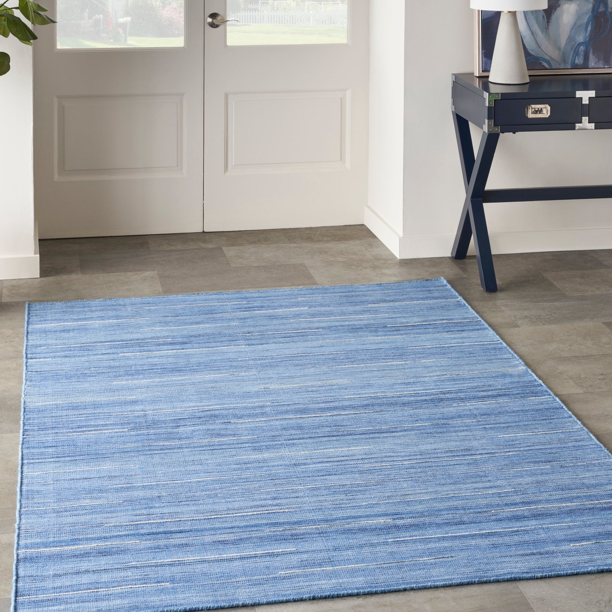 Blue striped area rug in entryway with blue tones on gray tile; white double doors behind, navy console table with lamp.