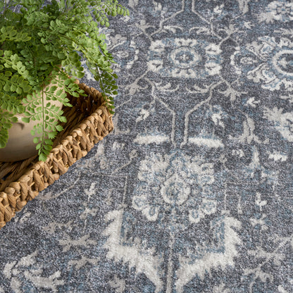 Blue-gray oriental rug with white floral medallions; fern in a woven basket rests on the rug's top-left edge.