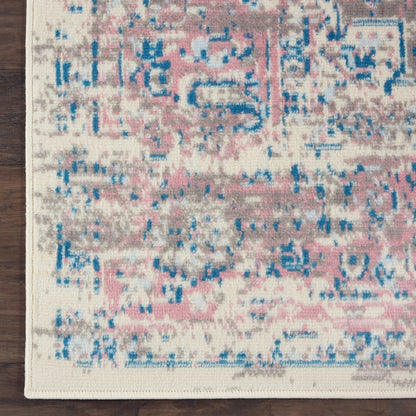 Distressed oriental rug with pink, blue & beige hues, abstract medallion pattern, cream border on dark wood floor.