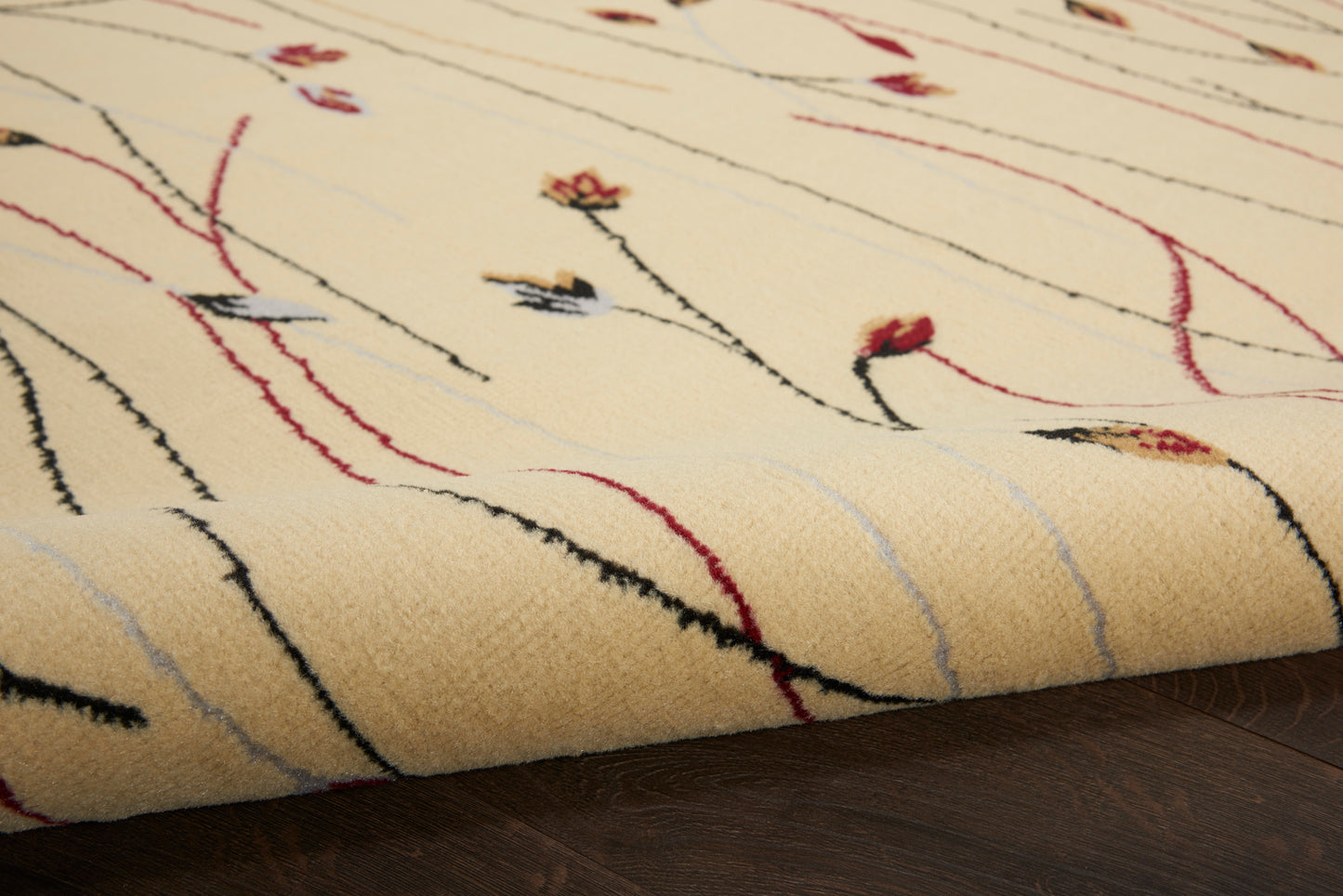 Beige rug with abstract red, black and blue lines and small floral accents, rolled on dark wood floor.