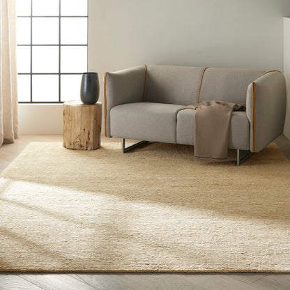 Light gray modern sofa with orange piping, beige throw, wooden stump side table and black vase in sunlit living room.