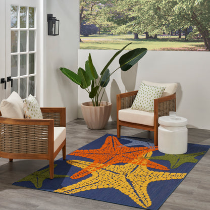 Outdoor patio with two brown wicker armchairs, white cushions, vibrant starfish rug, large potted plant, white side table.