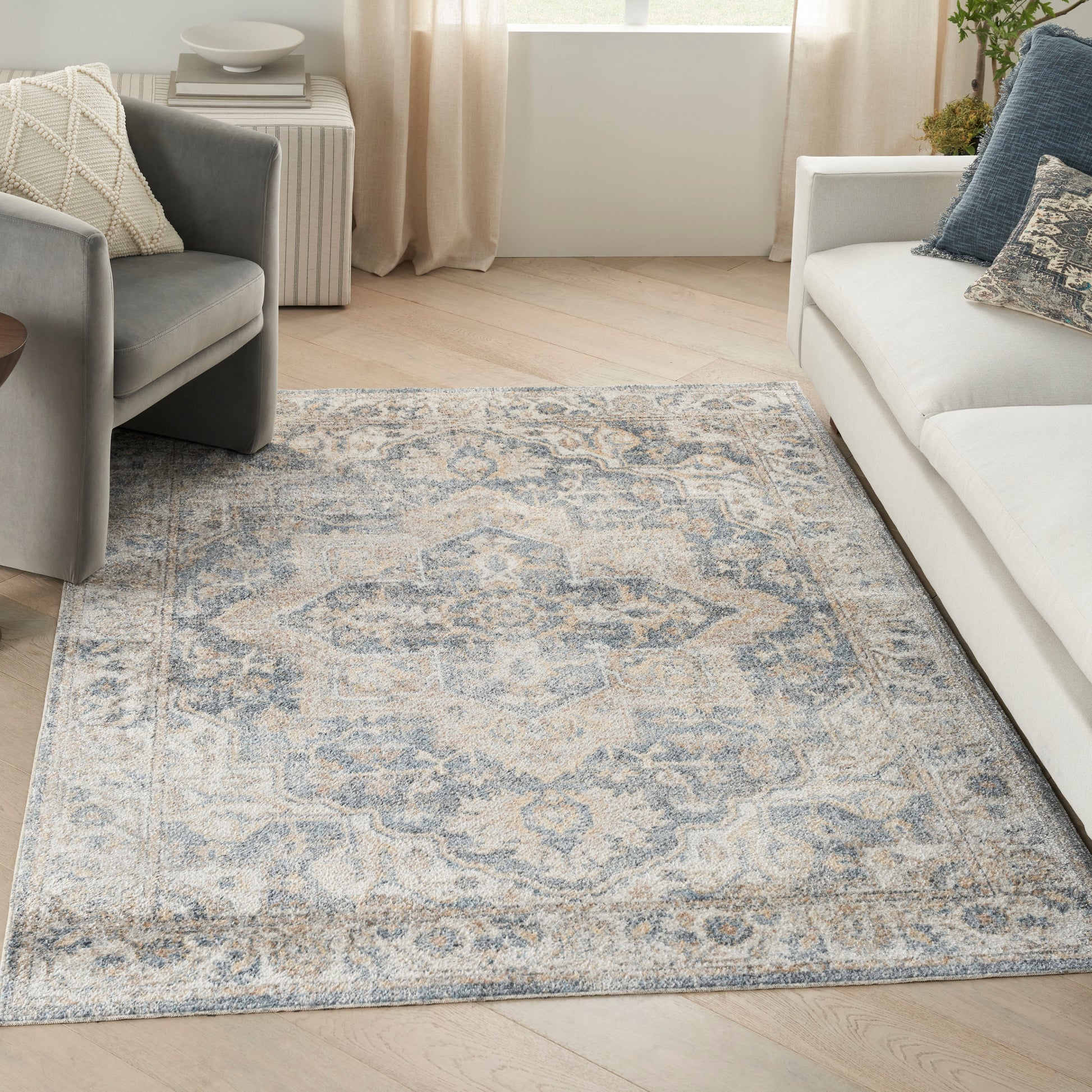 Soft blue-beige oriental area rug on a light wood floor beside a gray armchair and white sofa.