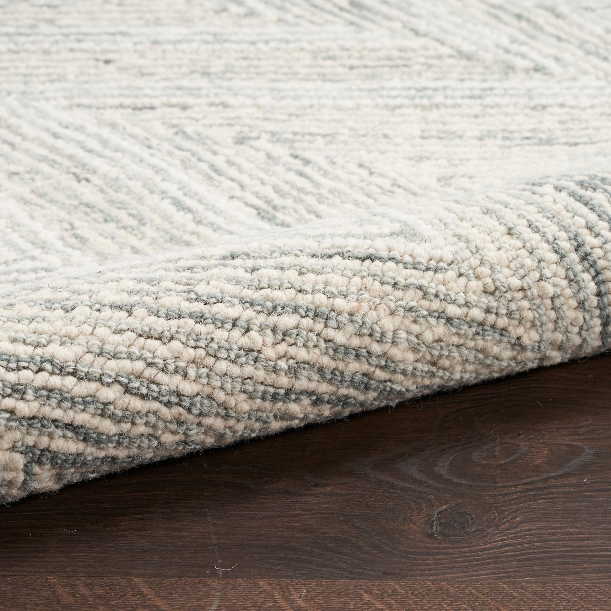 Light gray cream textured rug with subtle chevron pattern and rolled edge on dark wood floor.