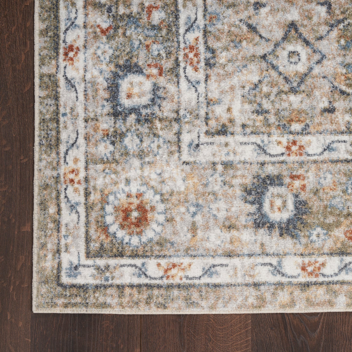 Traditional Persian-style area rug with cream field, blue and orange floral medallions, blue border on dark wood floor.