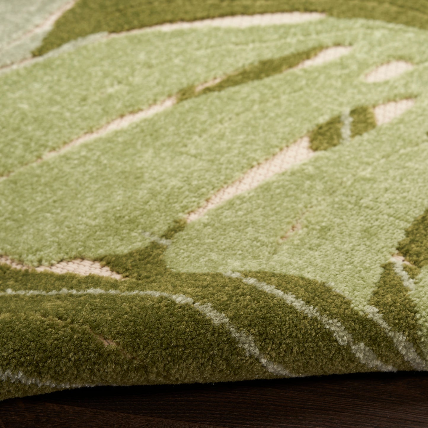 Close-up of a green outdoor rug with abstract light and dark olive patterns on a dark wooden deck, 6' x 9'.