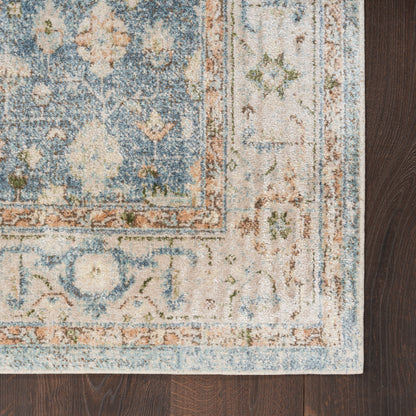 Rectangular oriental rug in blue, ivory, and rust with a distressed floral border on dark wood floor.
