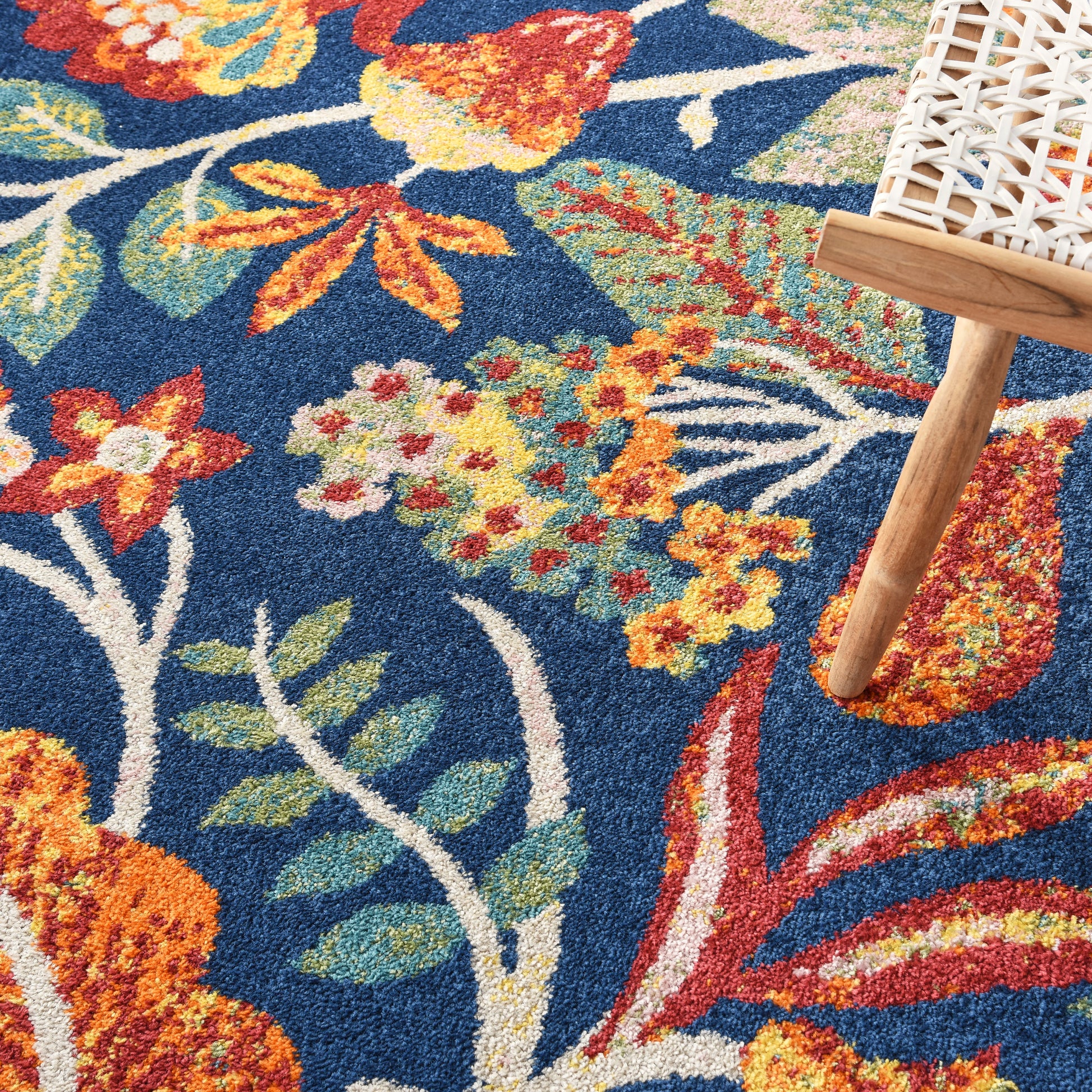 Blue floral rug with orange, yellow, and green blossoms; wooden chair leg resting on edge.