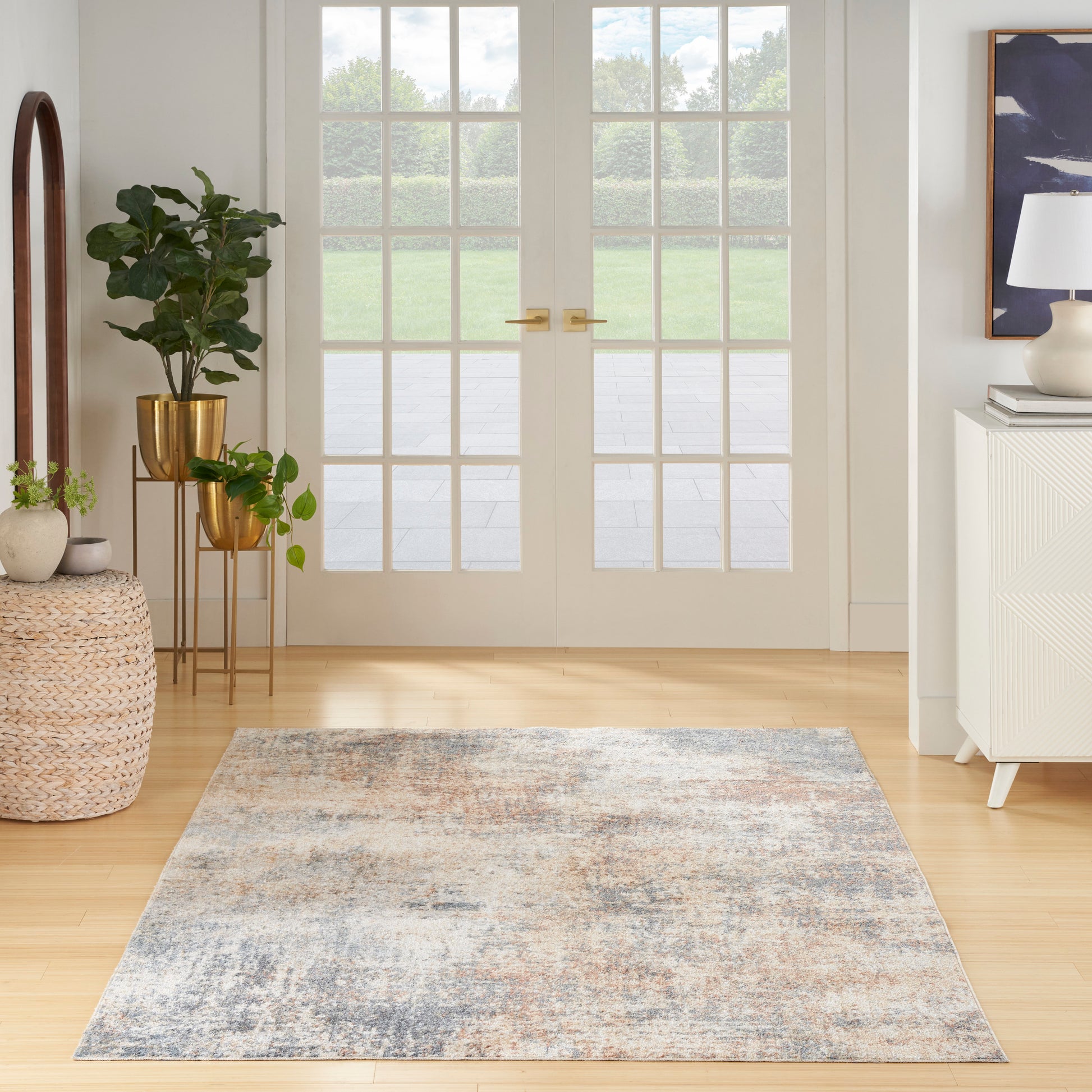 Rectangular blue-gray distressed area rug on light wood floor in a bright living room with plants and glass doors.