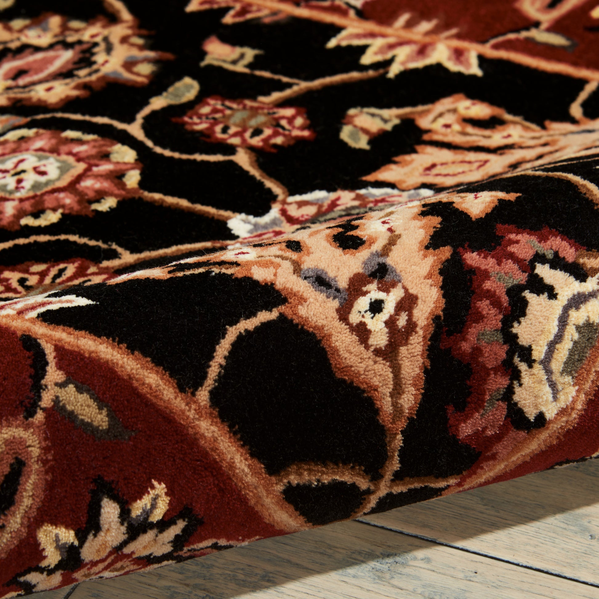 Close-up of a red, black and cream floral Persian-style rug with ornate vine motifs on a wooden floor.