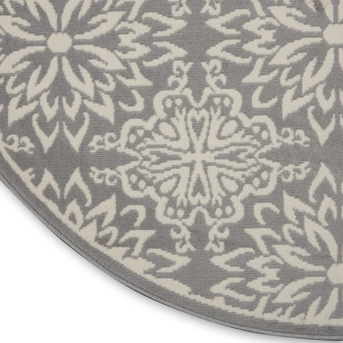 Round gray rug with white geometric floral/mandala motifs; soft woven texture, decorative for living room.