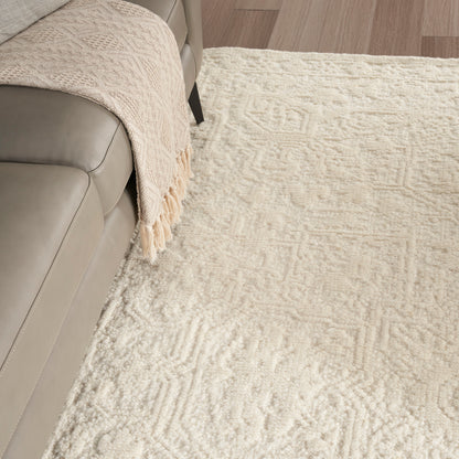 Cream textured area rug with subtle geometric pattern beside a beige leather sofa and a cream fringed throw.