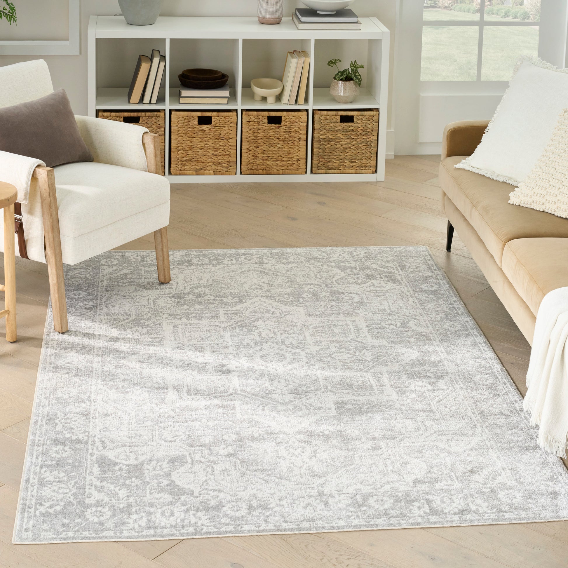 Light gray patterned area rug on light wood floor with beige sofa, white chair, and white cubby shelf with wicker baskets.