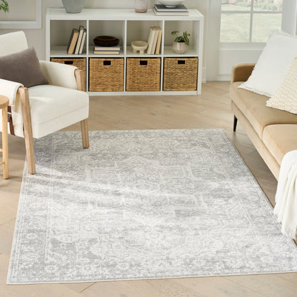 Light gray patterned area rug on light wood floor with beige sofa, white chair, and white cubby shelf with wicker baskets.