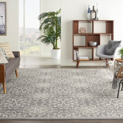 Living room with gray patterned area rug, mid-century sofa, wooden open shelving, gray accent chair, tall plant, window.